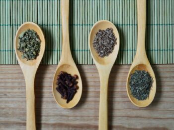 brown wooden spoon with herbs on top of green bamboo mat and brown wooden surface