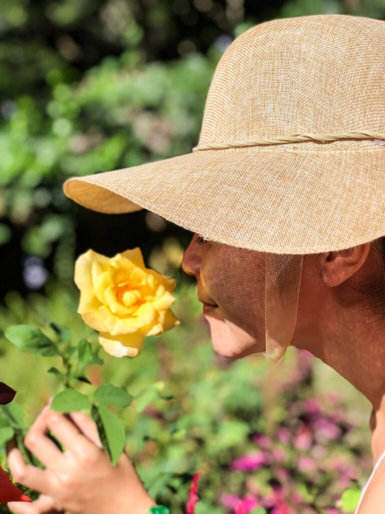 woman wearing sun hat smelling yellow rose