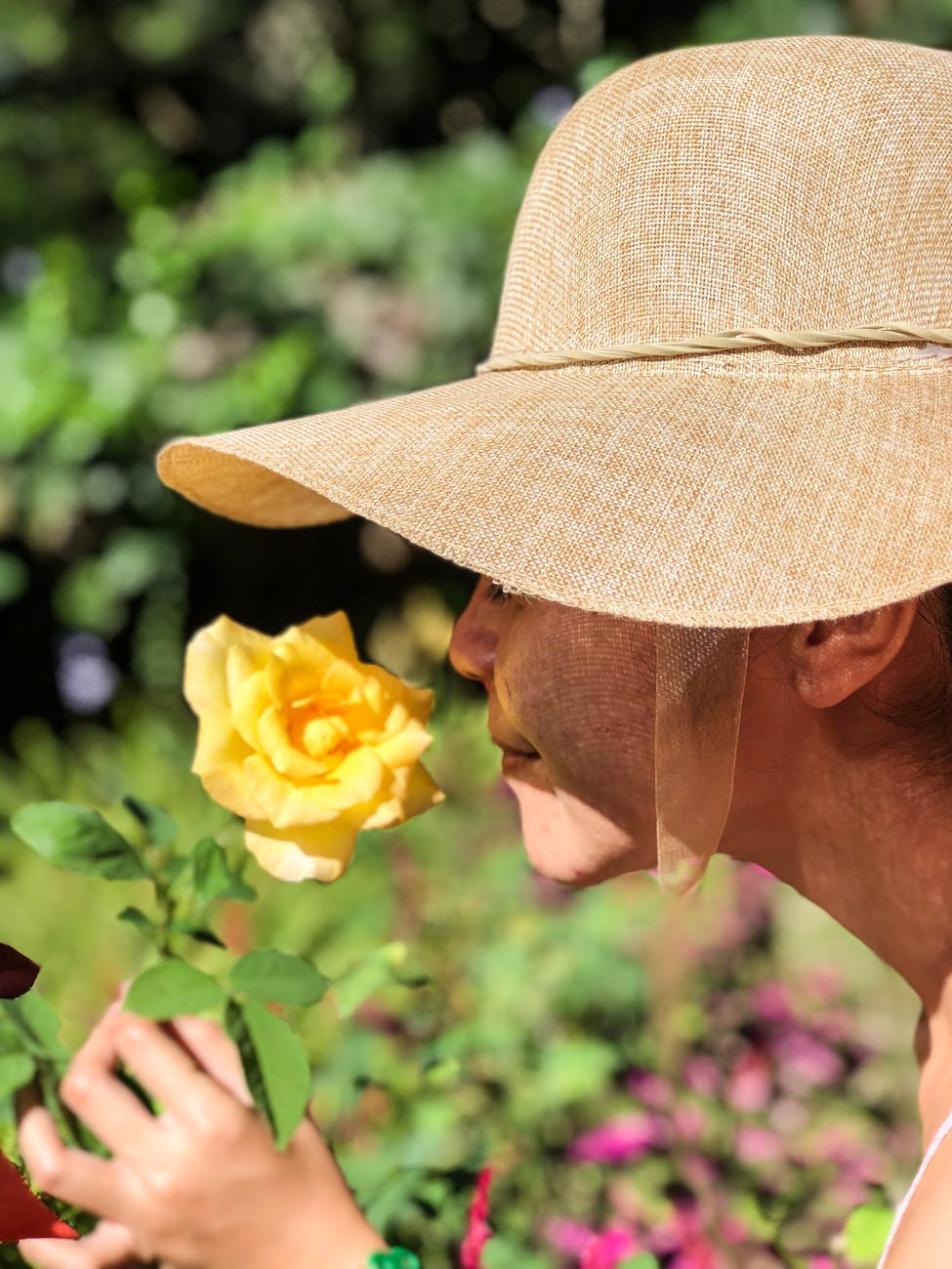 woman wearing sun hat smelling yellow rose