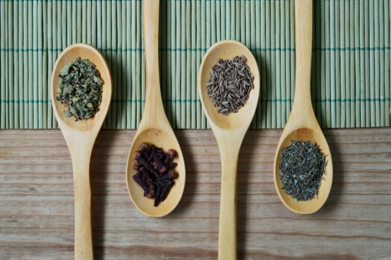 brown wooden spoon with herbs on top of green bamboo mat and brown wooden surface