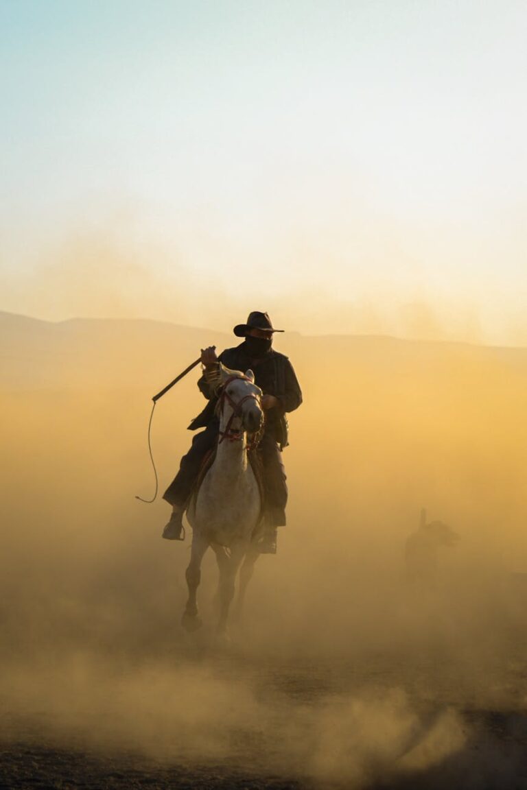 wrangler on horseback with a scarf over his face in a cloud of dust