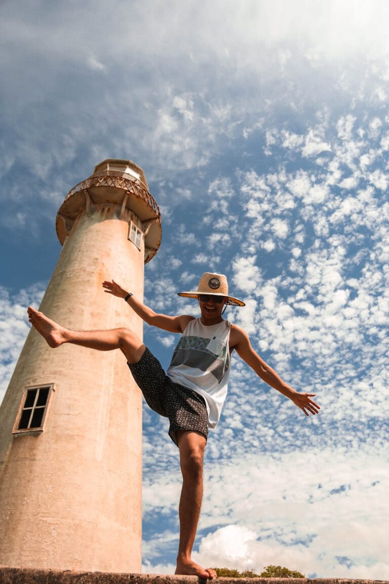 unrecognizable tourist dancing near old lighthouse under cloudy sky