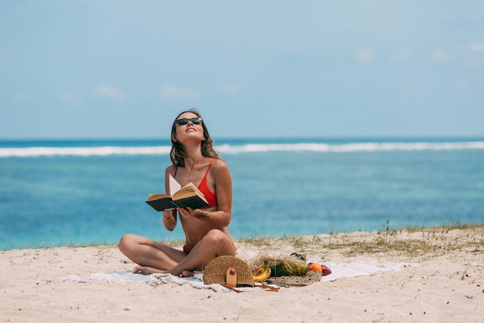a woman at the beach holding a book while looking up