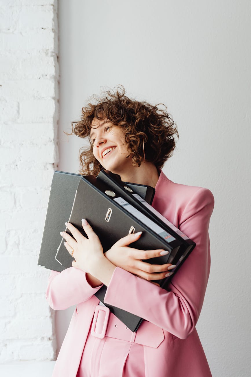 woman wearing pink suit hugging documents in binders
