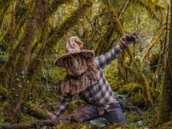 person dressed in a scarecrow halloween costume posing in a forest