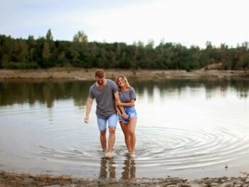 couple wearing grey t shirts walking on shallow water and smiling