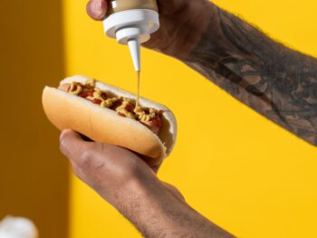 person putting mustard on hotdog