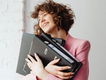 woman wearing pink suit hugging documents in binders